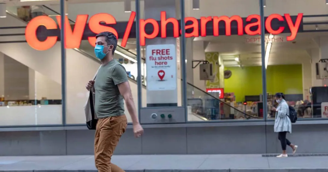 A person wearing a mask walking by a CVS pharmacy
A person wearing a mask walking by a CVS pharmacy