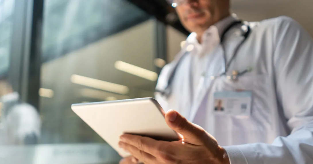
  Doctor holding a tablet while in a lab coat with a stethoscope around their neck 
