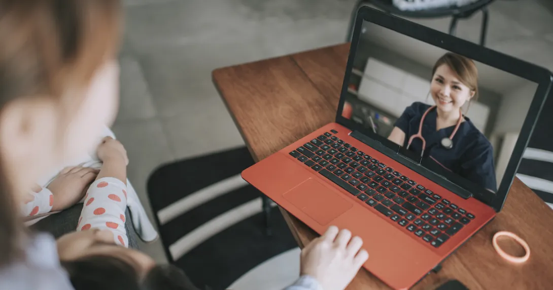 Two individuals sitting on a couch looking at a computer that is on a coffee table with a healthcare professional on the screen