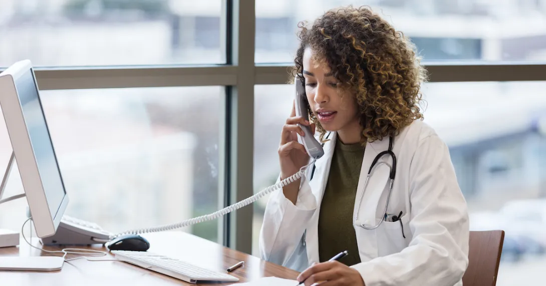 A doctor talking on a phone while taking notes.
A doctor talking on a phone while taking notes.