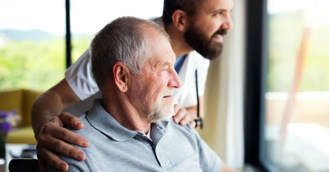 A person in a wheelchair and a healthcare provider standing beside them looking out a window
A person in a wheelchair and a healthcare provider standing beside them looking out a window