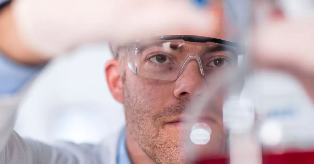 Scientist in a laboratory wearing safety goggles and putting something in a beaker Scientist in a laboratory wearing safety goggles and putting something in a beaker