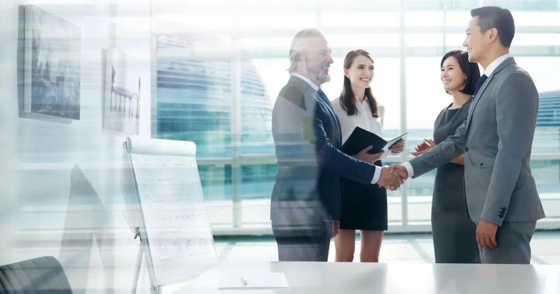 People standing in a room in front of a window while shaking hands