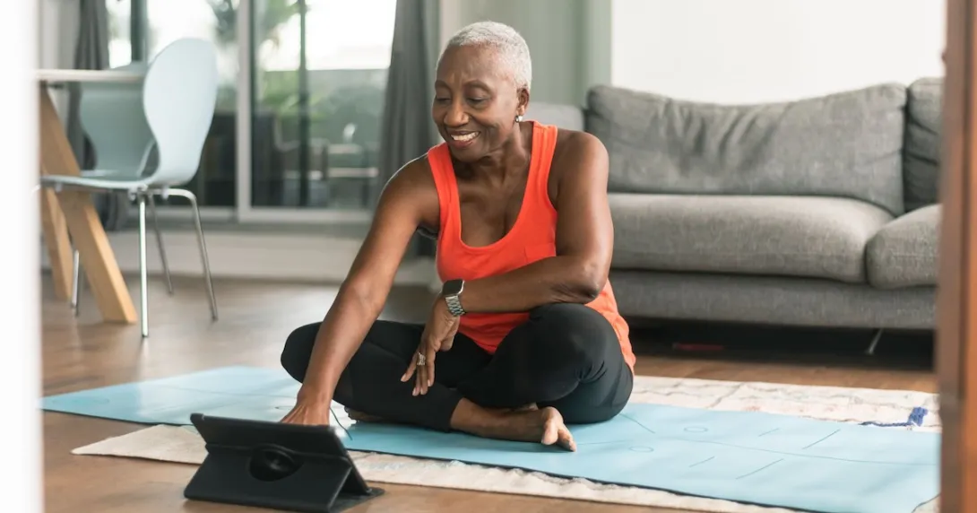 Person sitting on the floor in a room wearing exercise clothes and looking at a tablet Person sitting on the floor in a room wearing exercise clothes and looking at a tablet